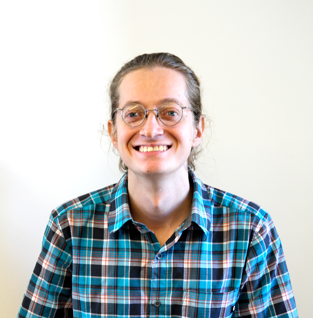 Logan Gaastra smiling, wearing round glasses and a plaid shirt