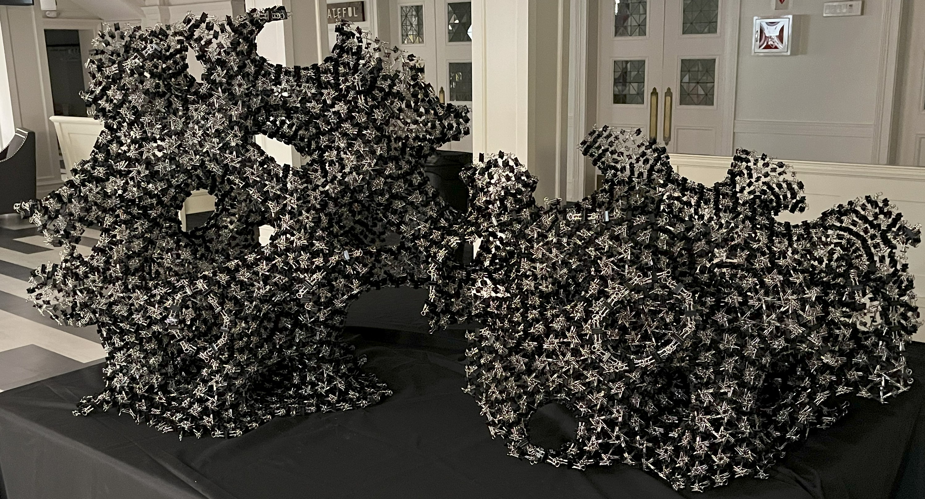 Unfinished Projects: intricate black and silver binder clip sculptures displayed on a black-covered table